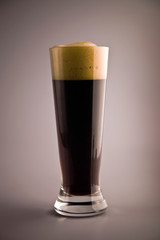 Glass of dark beer with froth against grey background