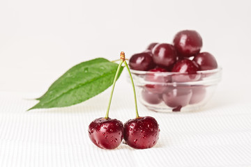 Still life with pair of red wet cherry fruit and glass bowl, on