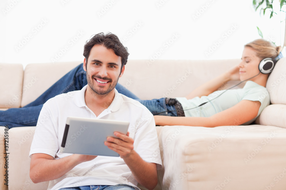 Poster Man using a tablet computer while his wife is listening to music
