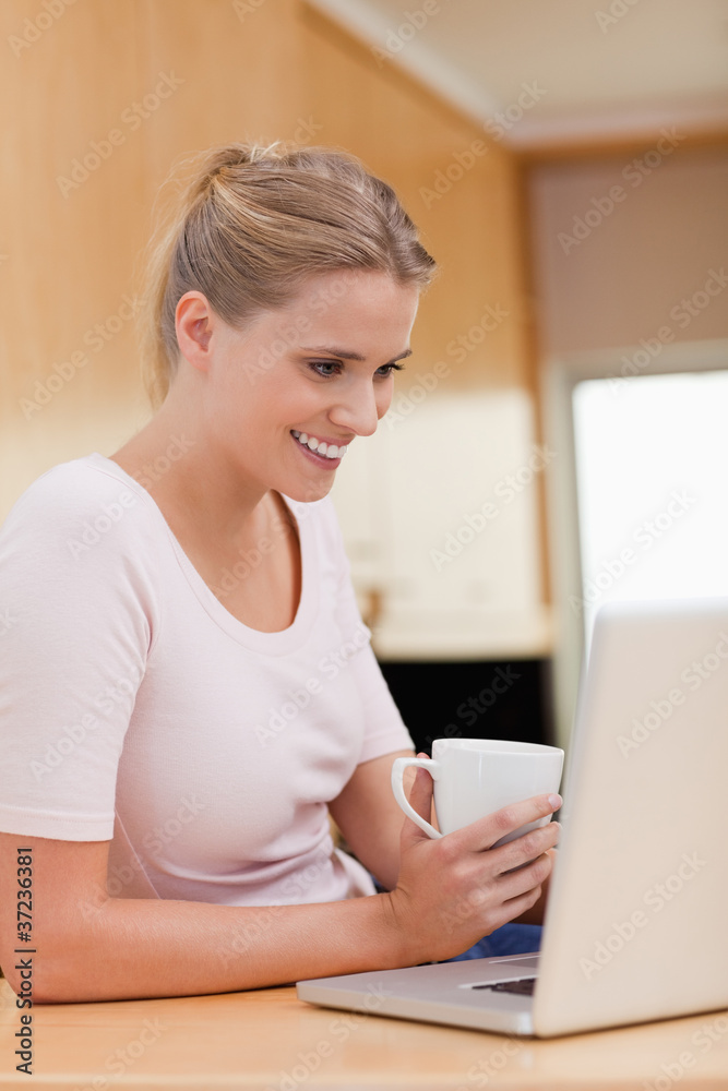 Poster Portrait of a woman using a notebook while drinking a cup of a t