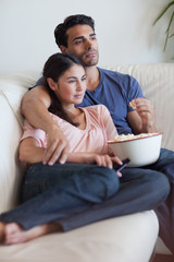 Obraz premium Portrait of a couple watching television while eating popcorn