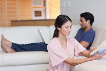 Woman reading a book while her fiance is using a laptop