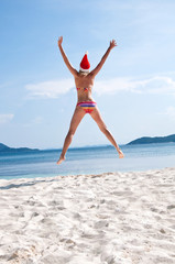 Young woman jump on the beach in santa's hat