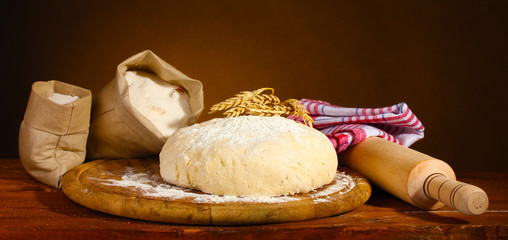 Dough and bags with flour on wooden table on brown background
