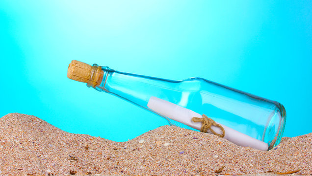 Glass bottle with note inside on sand on blue background