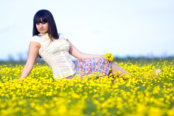 brunette beautiful girl lying in a field of yellow flowers