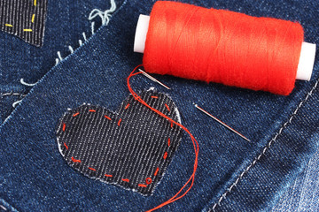 Heart-shaped patch on jeans wiht needle and thread closeup