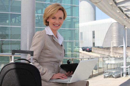 Businesswoman smiling on laptop outside airport