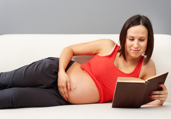 pregnant woman lying on sofa and reading book