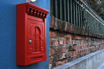 Red post box on brick wall and iron fence