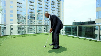 Ethnic Businessman Practicing Golf on City Office Roof - Powered by Adobe