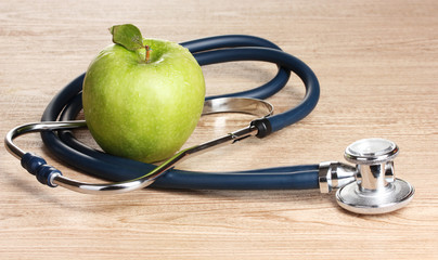 Medical stethoscope and green apple on wooden background