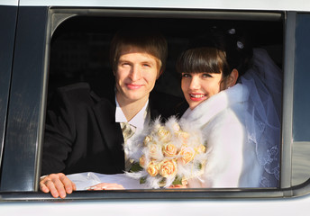 smiling groom and bride with bouquet sitting in limousine