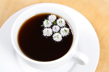 Cup of tea with flowers of peppermint floating in it