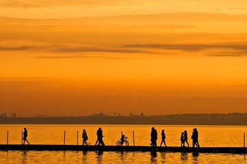 Fototapeta premium Group of people walking and biking on boardwalk at sunset