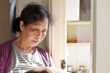 Fototapeta na wymiar A 50s asian woman reading newspaper at home