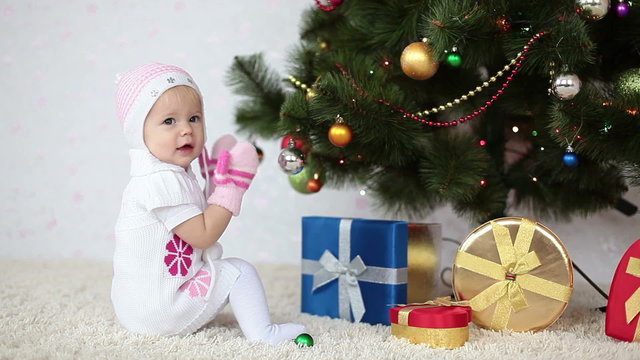 Baby girl sitting on the floor near the Christmas Tree