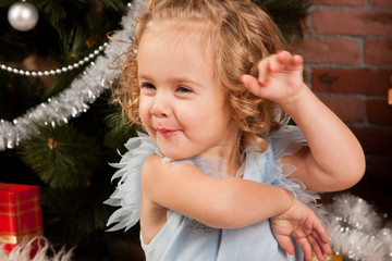 Little girl in nice dress  sitting near Christmas tree