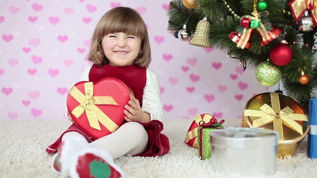 A girl on the floor near a Christmas tree with gift in hand