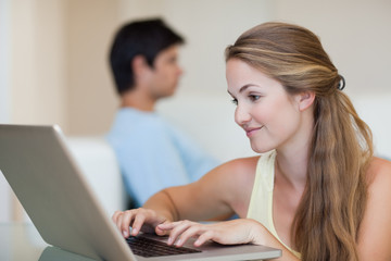 Woman using a laptop while her fiance is sitting on a couch