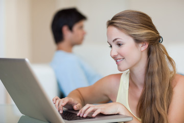 Woman using a laptop while her fiance is sitting on a sofa