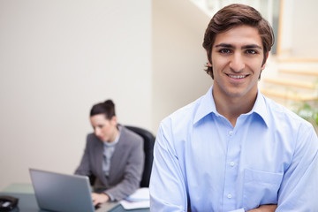 Smiling businessman with colleague on her laptop behind him