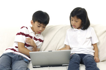 Young children sitting on couch at home, using laptop