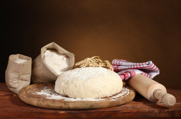 Dough and bags with flour on wooden table on brown background