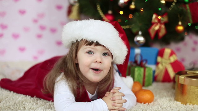 Baby girl in a santa hat lying on the floor. Looking at camera
