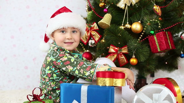 Girl in santa hat sitting beside a Christmas tree