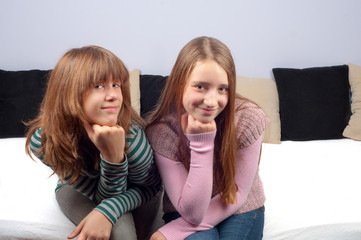 Two pretty teenage girls sitting on the bed and smiling
