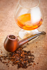 Glass of cognac and pipe with tobacco on linen canvas background
