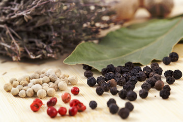 white ,black and red peppercorns and other herbs close up on wooden surface