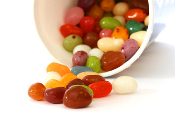 Colourful candies in a pot and scattered on white background