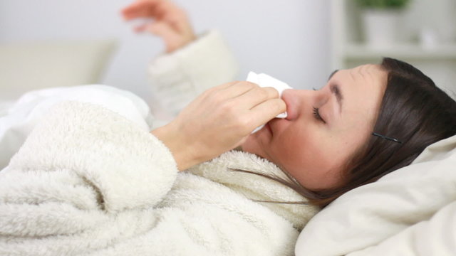 Sick woman blowing nose and putting thermometer in mouth
