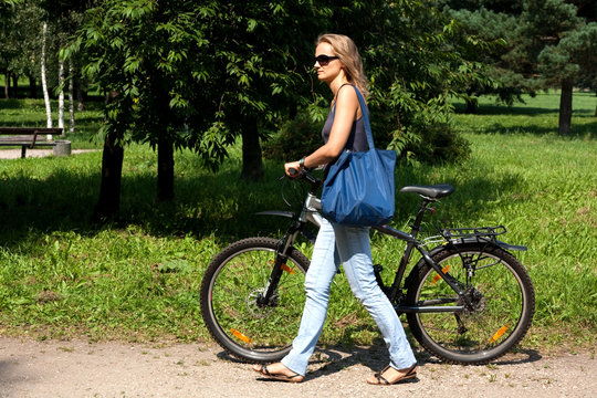 Красивая девушка идет в магазин с велосипедом и сумкой