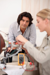 Woman repairing computer and man sitting on a sofa