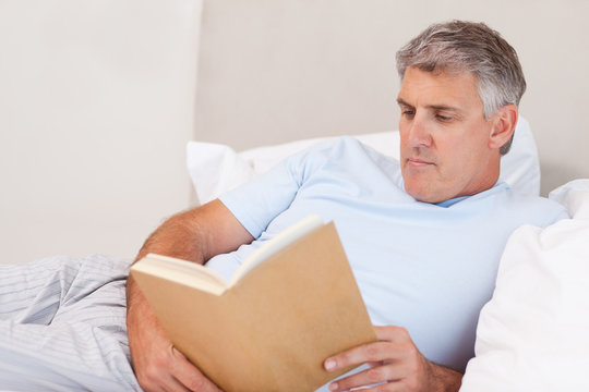 Mature Man Reading Book In Bed