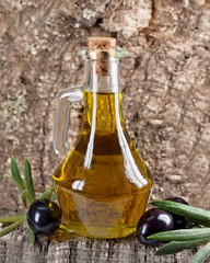 Olivenölflasche vor Kork mit schwarzen Oliven und Blättern