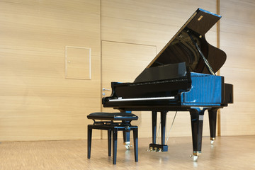 opened black grand piano with stool on a wooden concert stage