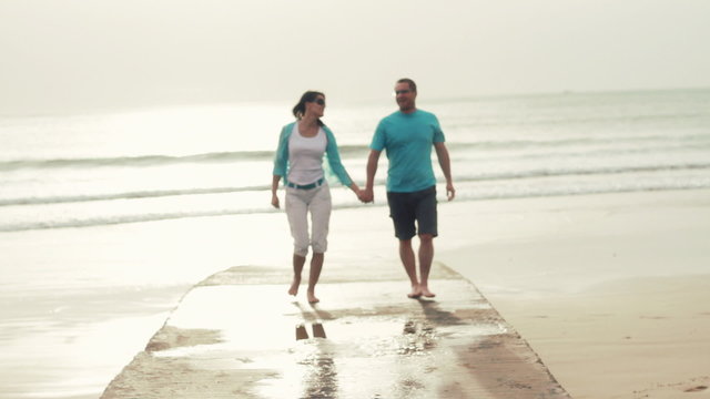 Young happy couple walking towards camera at the beach
