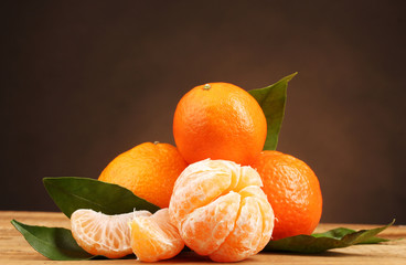 tangerines with leaves on wooden table on brown background