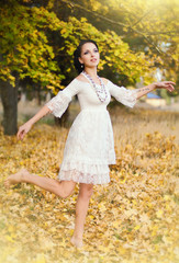 beautiful brunette in a white dress walks on autumn park