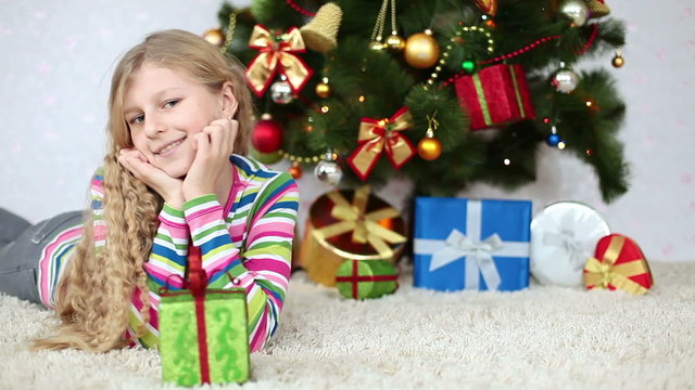 Happy girl with a gift lies near the Christmas Tree