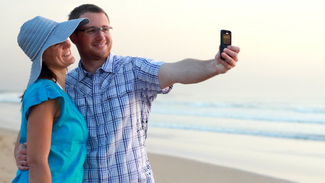 Happy couple taking photo with cellphone on the beach