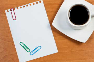 Cup coffee on table and torn sheet with clips.