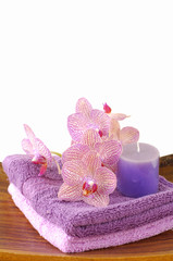 Pink orchid and towel and candle in wooden bowl of on mat