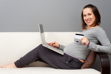 pregnant woman holding laptop and showing credit card