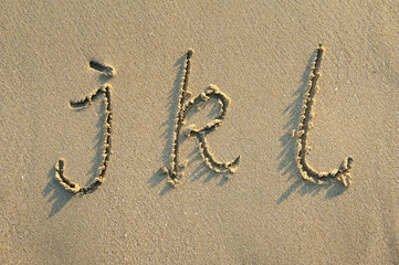 alphabet letters handwritten in sand on beach