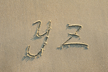 alphabet letters handwritten in sand on beach